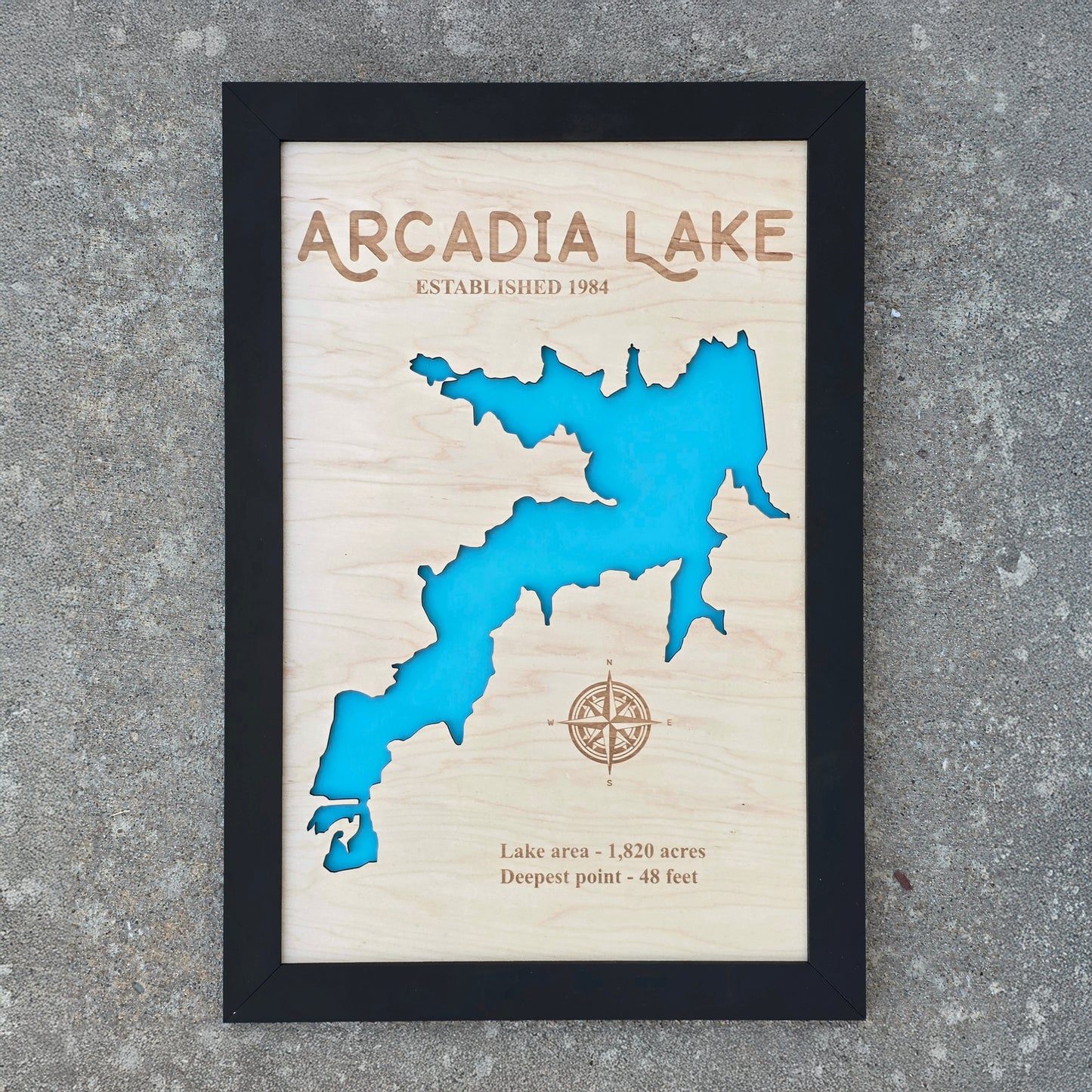 Framed Arcadia Lake wooden map wall art photographed outdoors, layered wood lake map with engraved lake name and compass detail