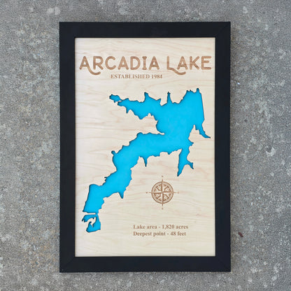 Framed Arcadia Lake wooden map wall art photographed outdoors, layered wood lake map with engraved lake name and compass detail