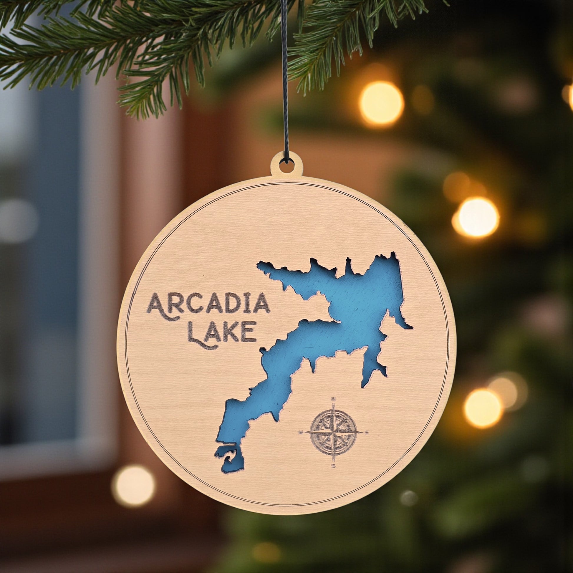Arcadia Lake layered wood ornament hanging on a Christmas tree, featuring laser-cut Oklahoma lake map with blue background and compass engraving.