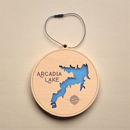 Flat lay of Arcadia Lake wooden ornament displaying detailed lake shoreline cutout, engraved name and compass, Oklahoma lake map ornament made from wood.