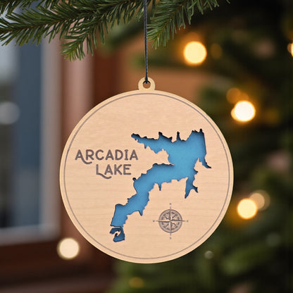 Arcadia Lake wooden ornament hanging on evergreen tree, laser cut wood lake map ornament with blue inlay used as Oklahoma lake Christmas decor or travel keepsake