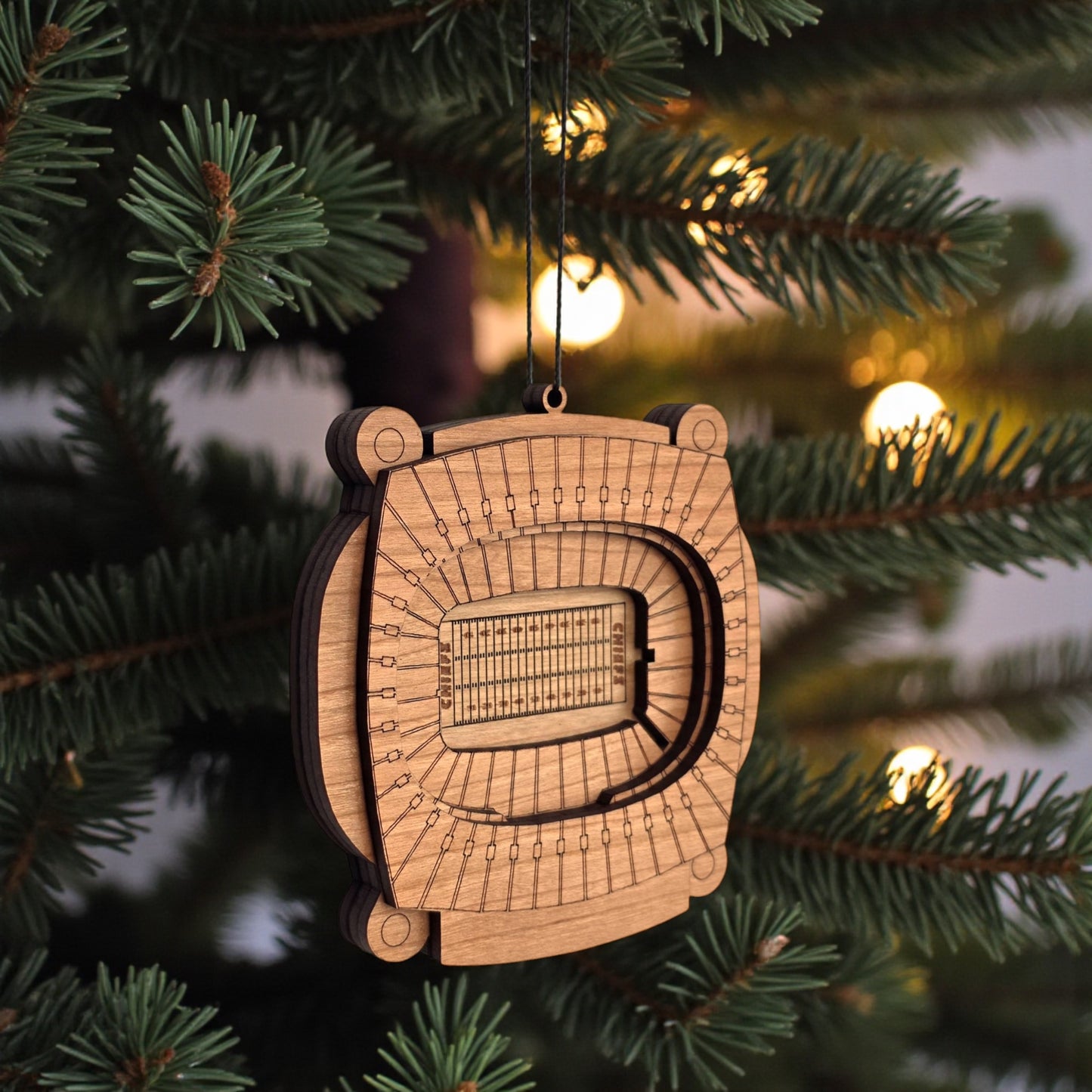 Angled view of Arrowhead Stadium wooden ornament hanging from black cord, layered wood Kansas City football stadium ornament for sports fan gift