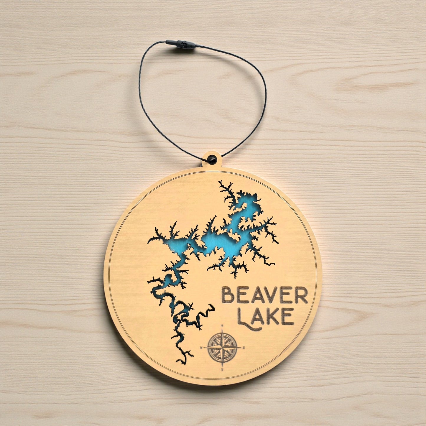 Flat lay of Beaver Lake layered wooden ornament showing engraved lake name, compass detail, and blue painted water layer beneath laser cut wood top