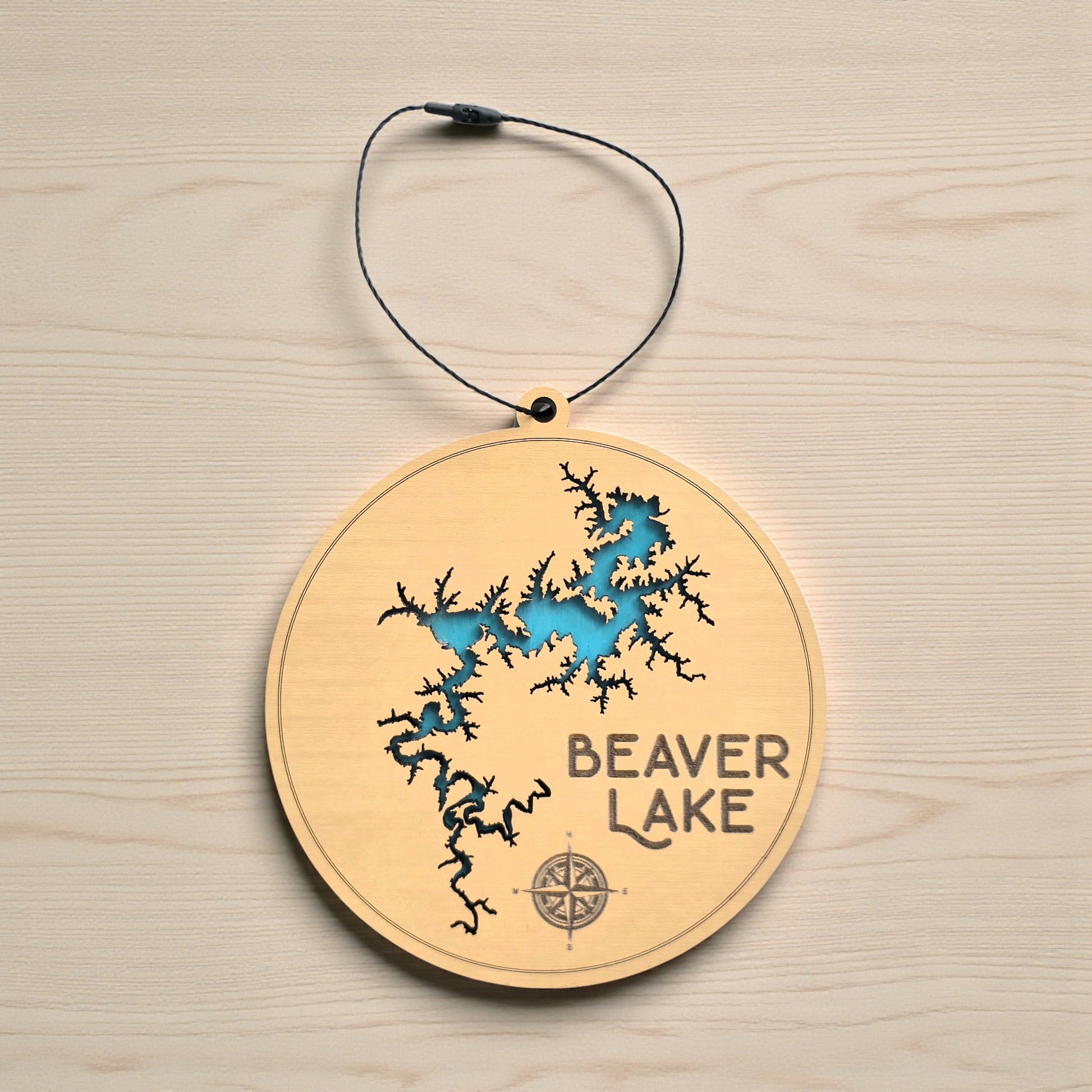 Flat lay of Beaver Lake layered wooden ornament showing engraved lake name, compass detail, and blue painted water layer beneath laser cut wood top