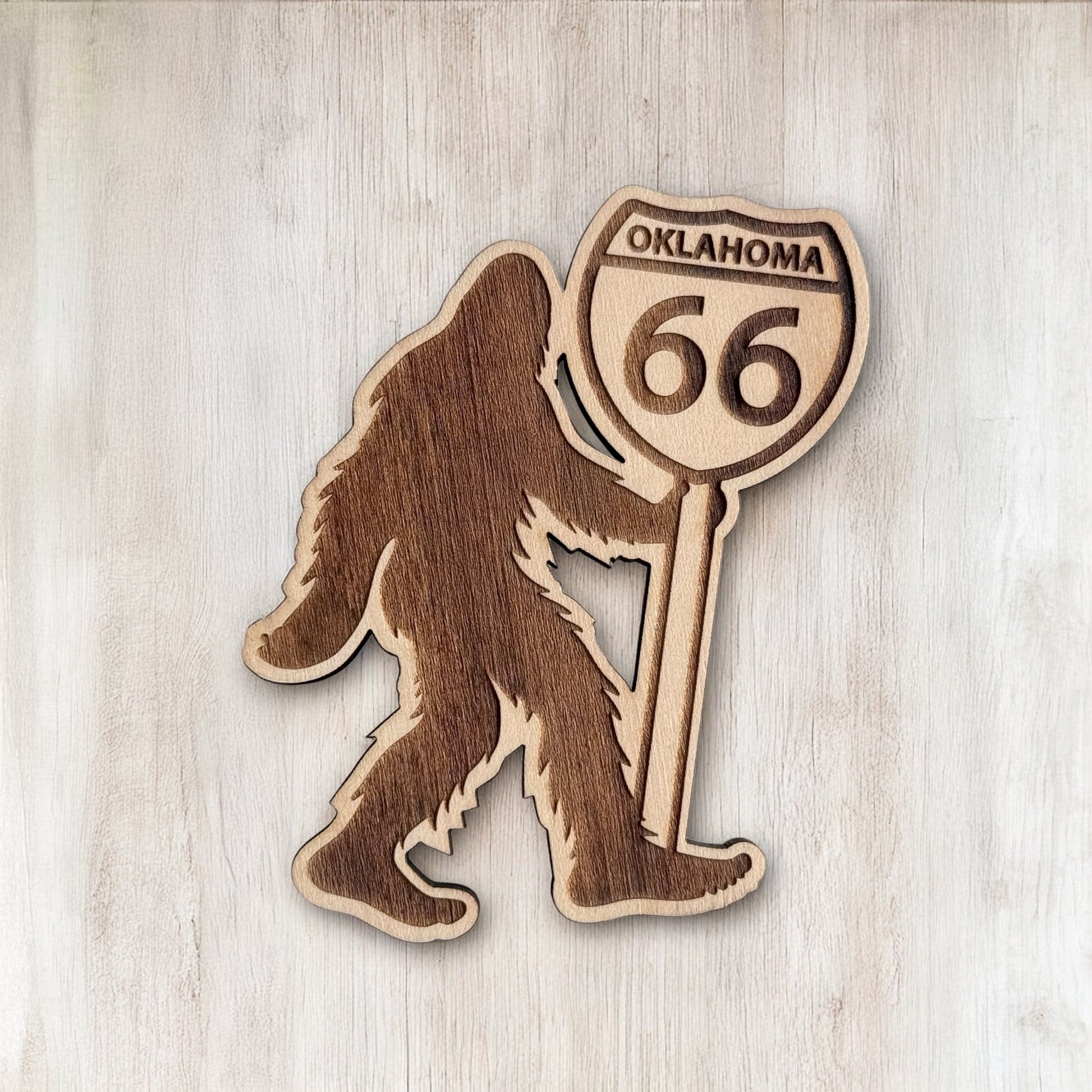 Bigfoot wooden magnet with Oklahoma Route 66 shield displayed on light wood background, laser cut Sasquatch magnet for Route 66 travel souvenir and Oklahoma gift