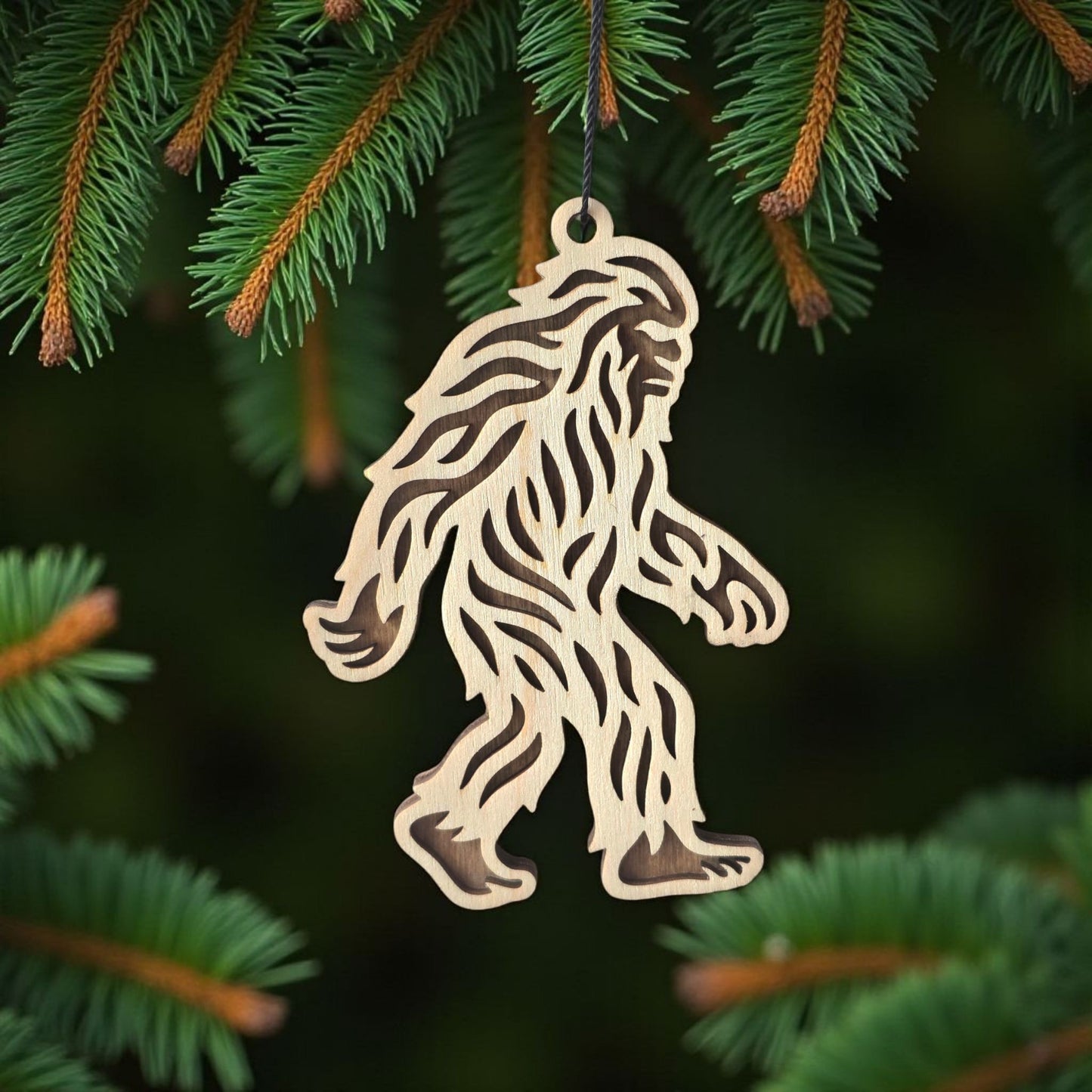 Bigfoot Sasquatch wooden ornament hanging on evergreen tree, laser cut wood ornament used as a forest themed holiday decoration
