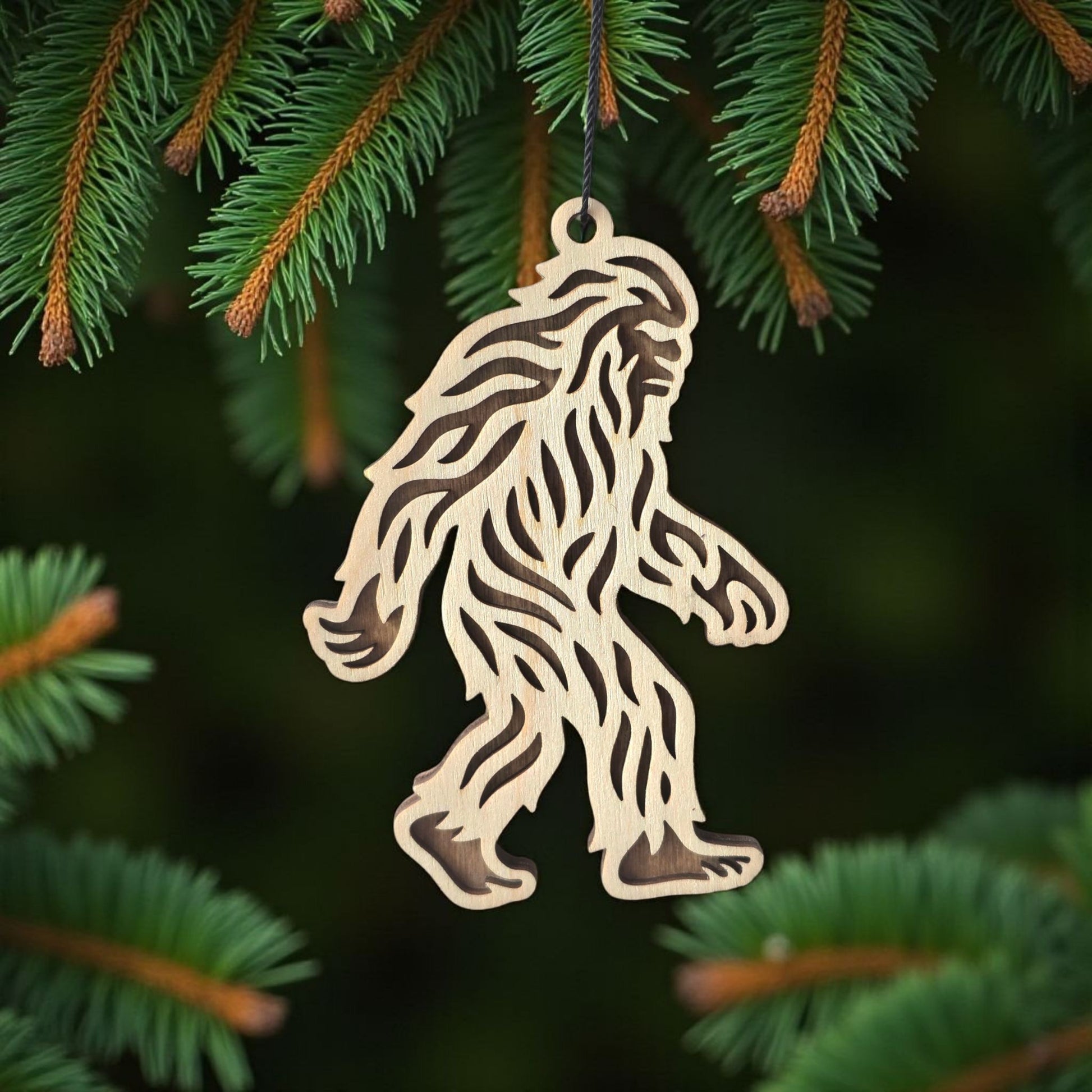 Bigfoot Sasquatch wooden ornament hanging on evergreen tree, laser cut wood ornament used as a forest themed holiday decoration