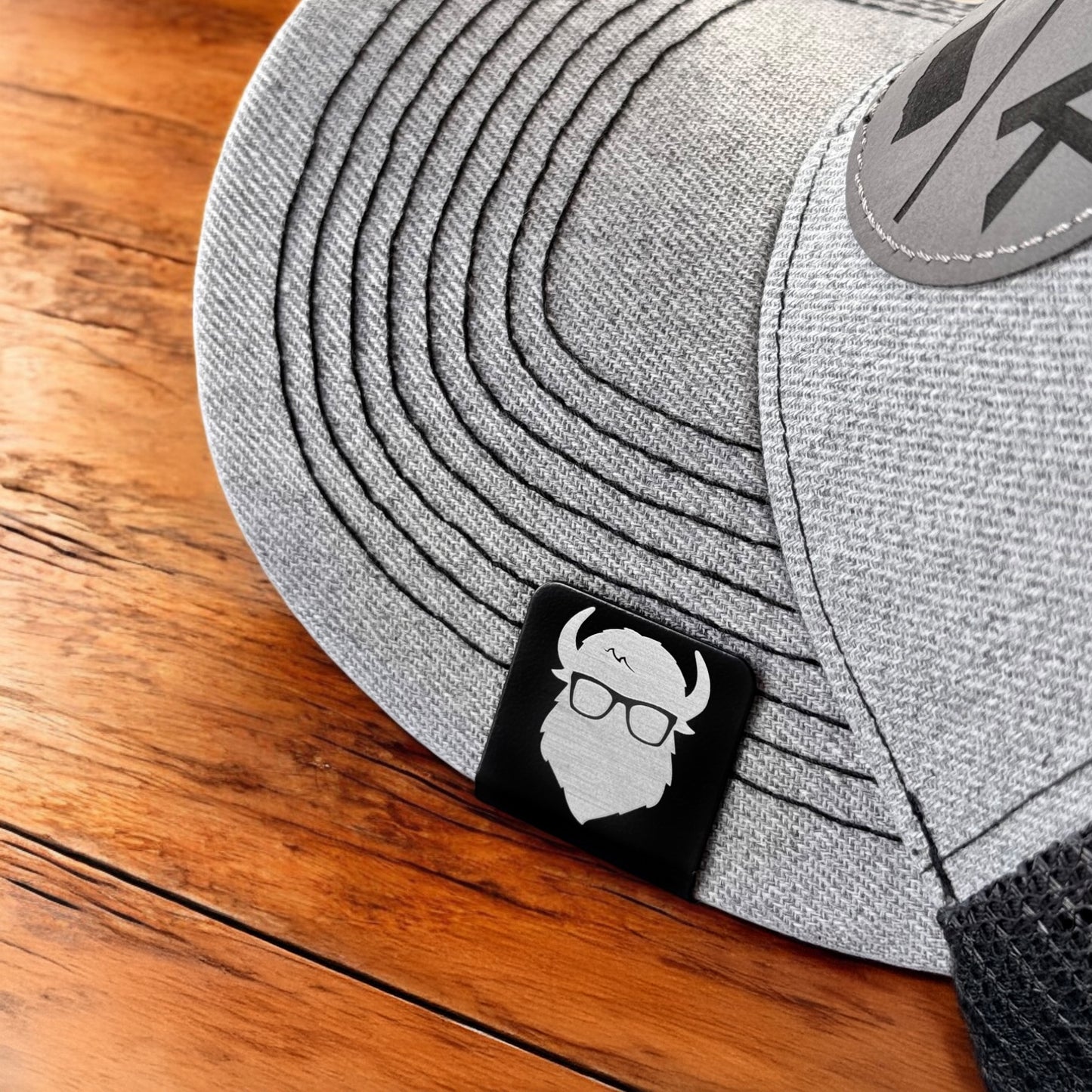 Aluminum Bison logo hat clip attached to the brim of a gray hat, square decorative clip worn as a subtle accessory