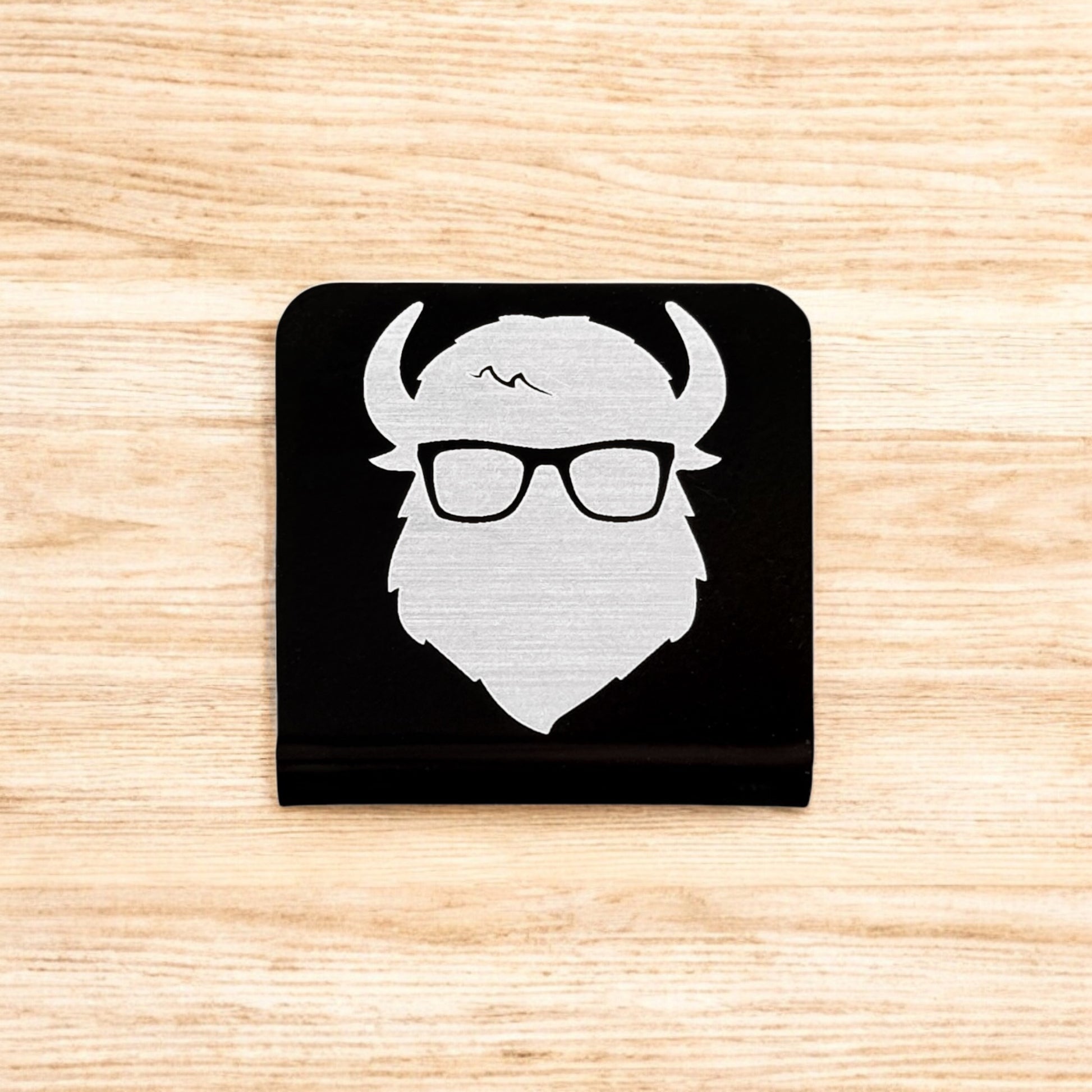 Flat lay of aluminum Bison logo hat clip showing square shape and brushed metal finish on black background