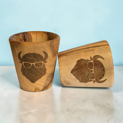 Two bison olive wood shot glasses showing natural wood grain variations and laser engraved buffalo wearing glasses, wooden souvenir drinkware and bison gifts