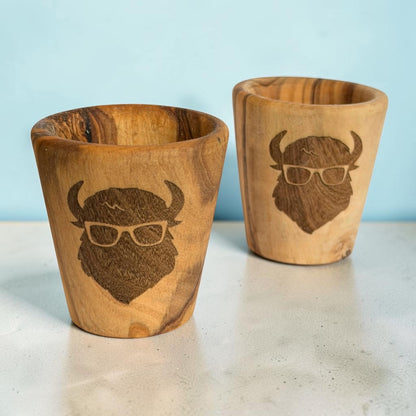 Pair of olive wood shot glasses with laser engraved bison wearing glasses, natural wooden buffalo gifts and travel souvenirs showing different wood grain patterns