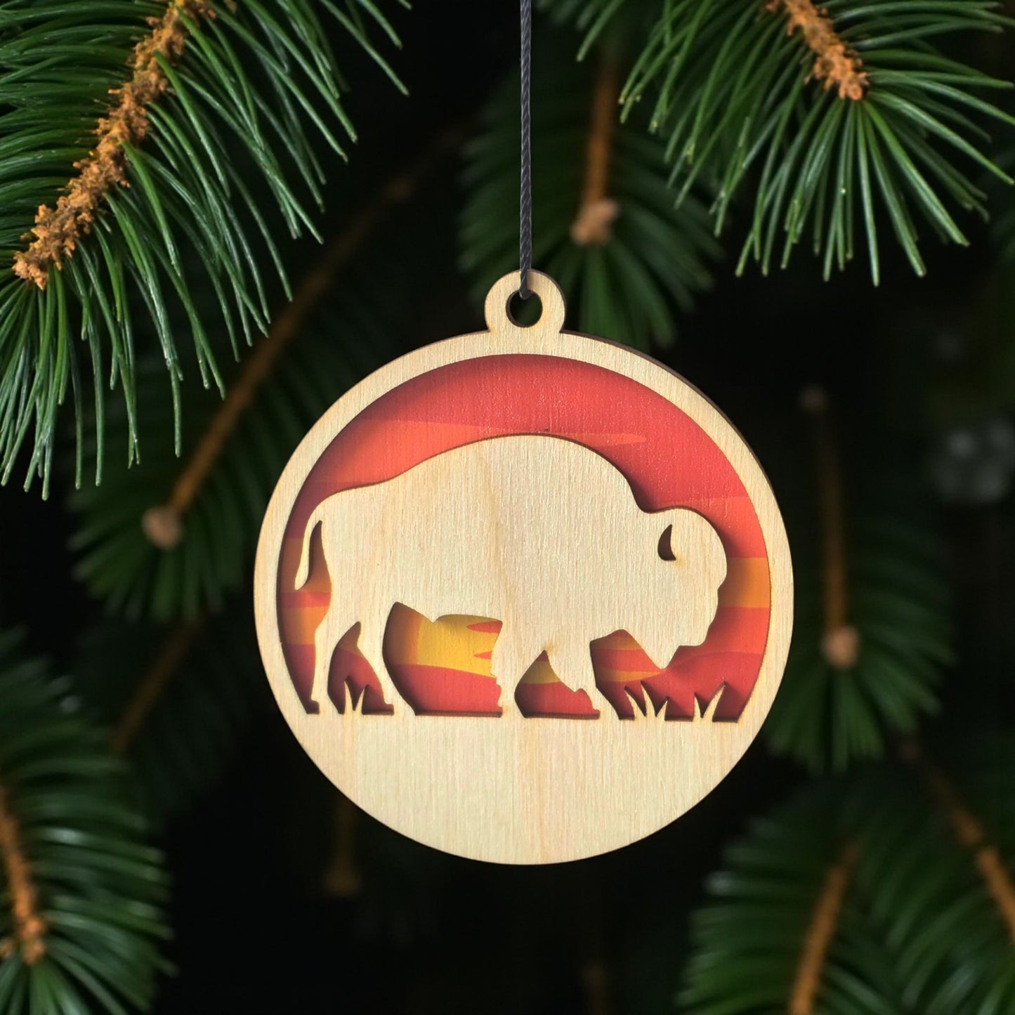 Bison sunset wooden ornament hanging on evergreen tree, layered wood wildlife ornament with warm sunset colors for rustic holiday decor