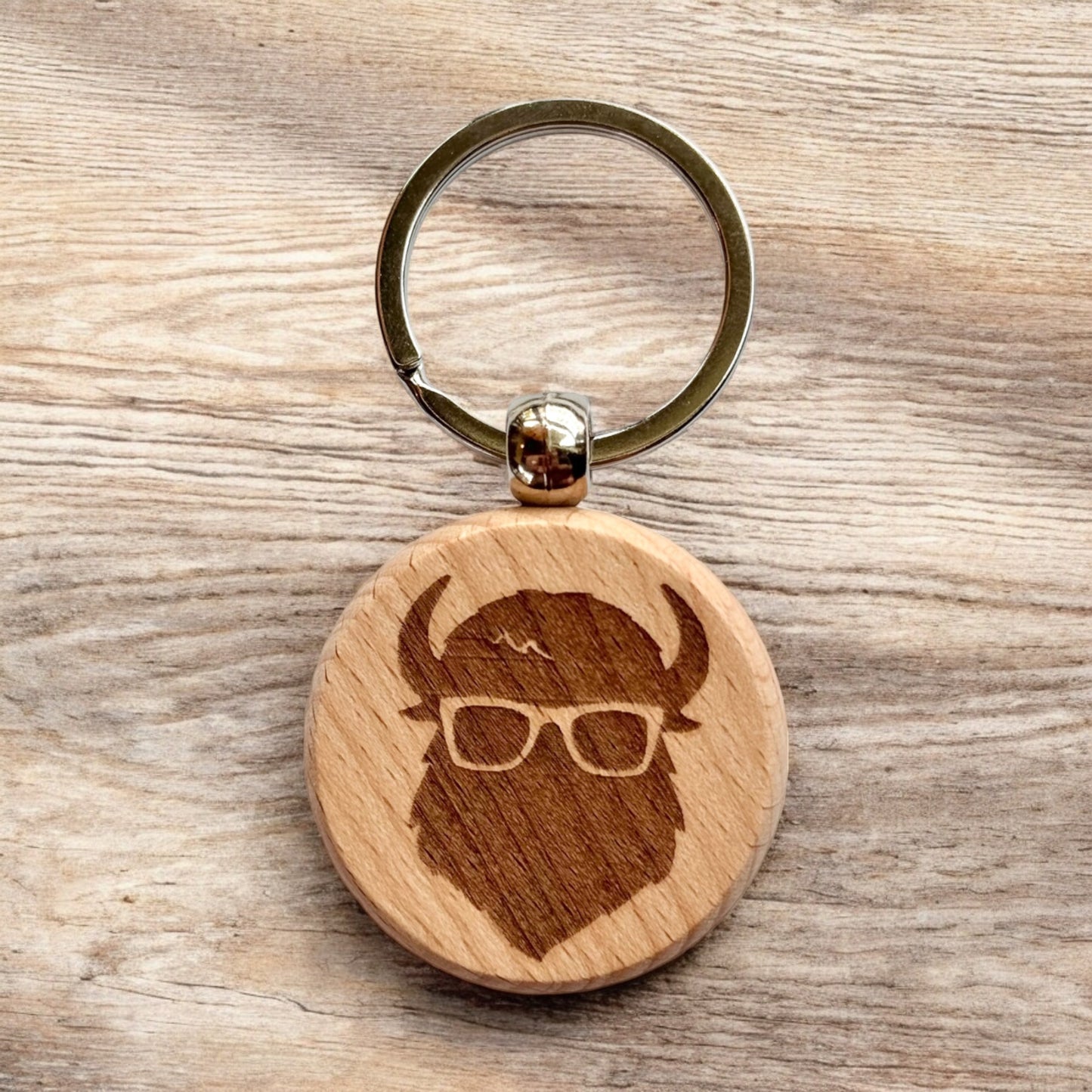Bison wooden keychain displayed on wood surface, laser engraved Curious Bison icon on round wooden keychain for everyday carry