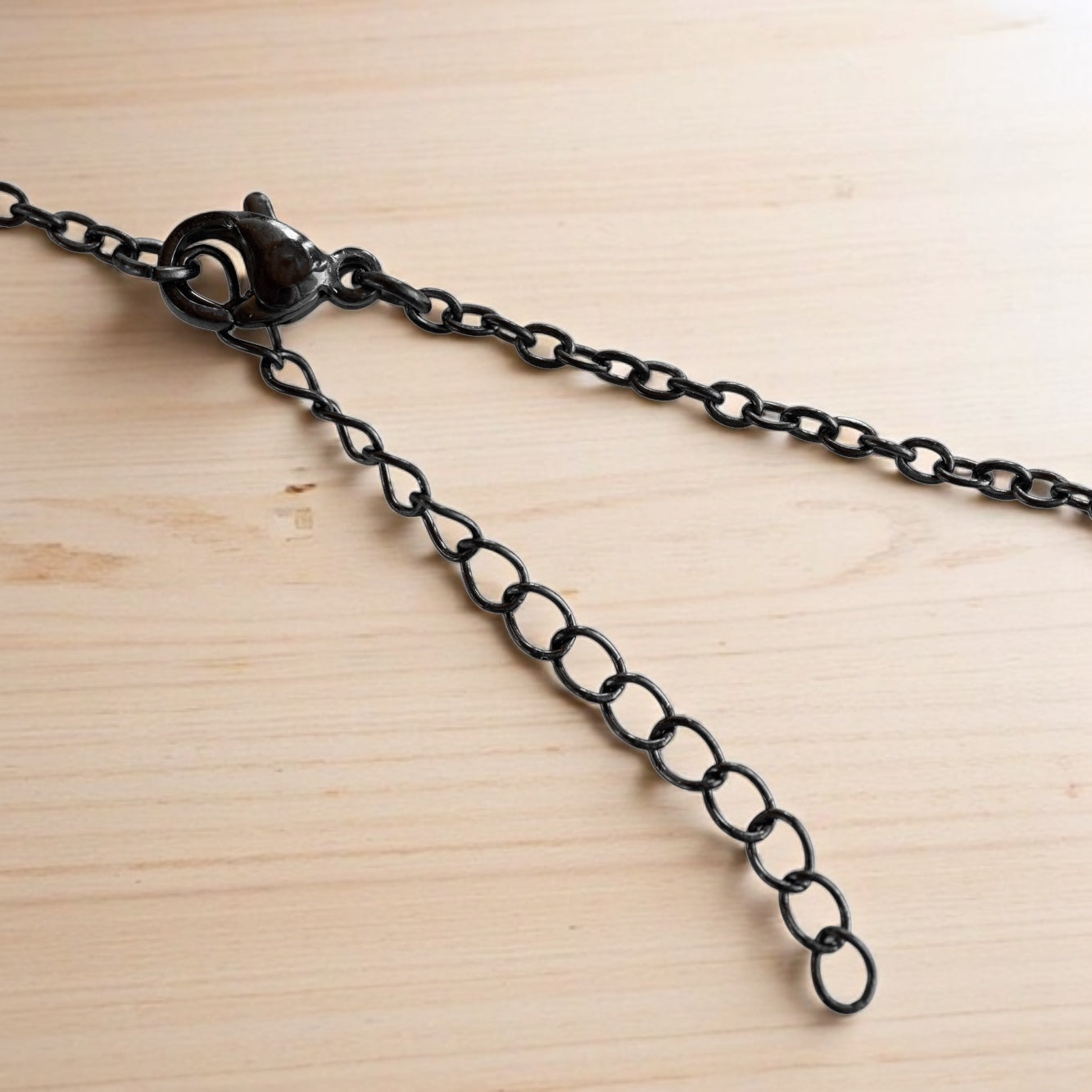 metal necklace chain extender featuring a lobster clasp, displayed on light wood background