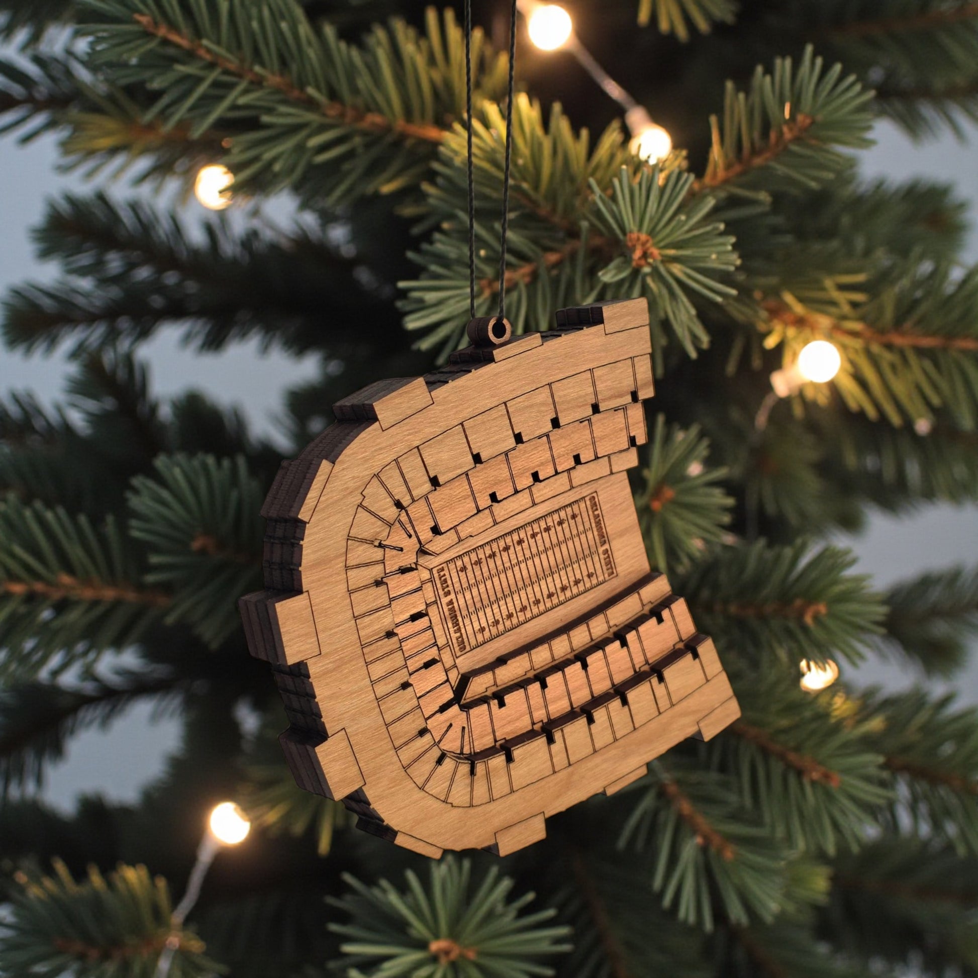 Angled view of Boone Pickens Stadium wooden ornament hanging from black cord, layered wood OSU football stadium ornament for sports fan gift