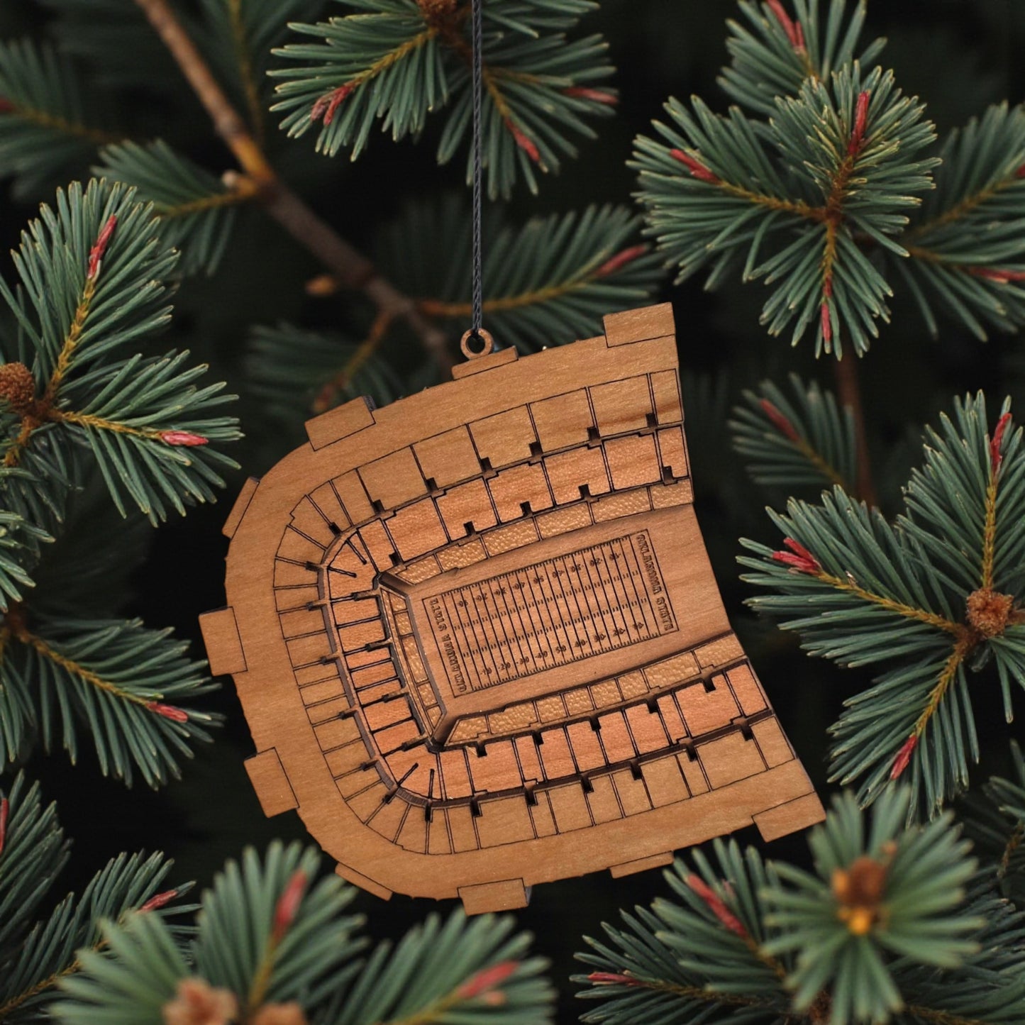 Boone Pickens Stadium wooden ornament hanging on evergreen tree with lights, laser cut OSU football stadium ornament used as college football Christmas decor