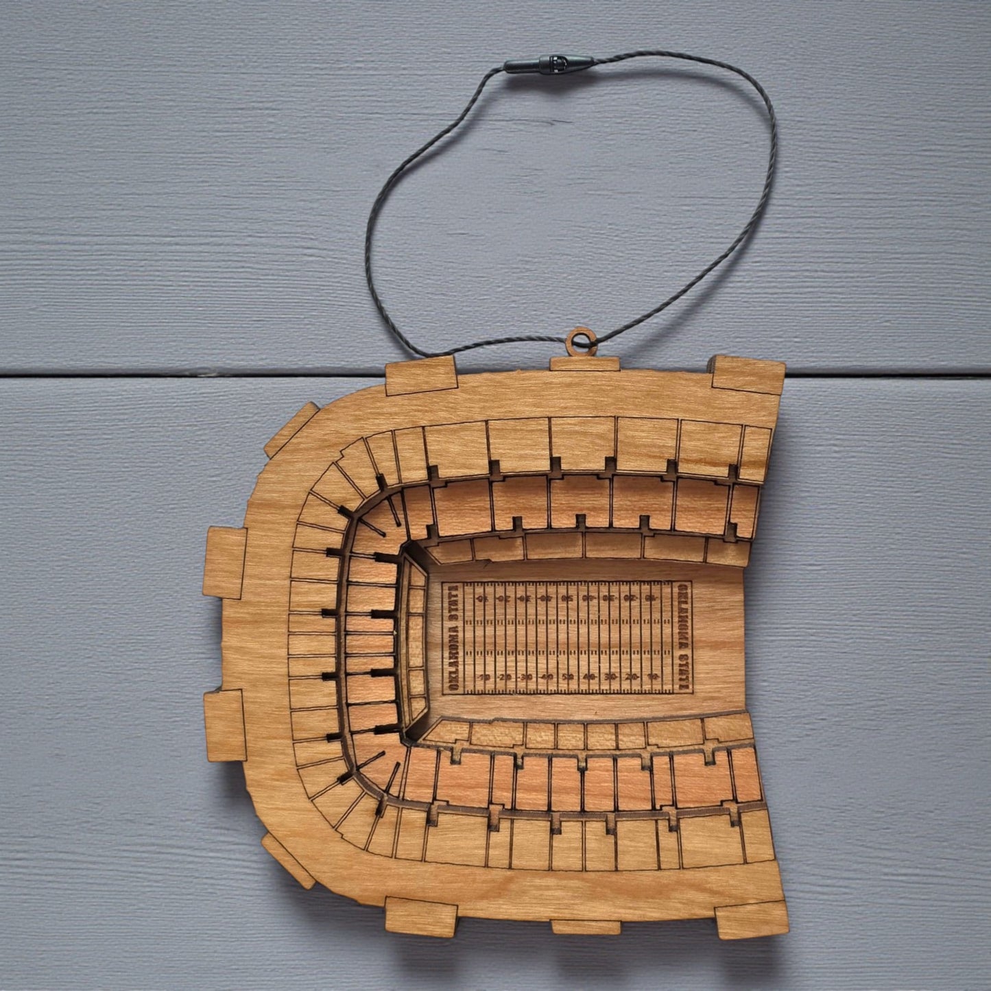 Flat lay of Boone Pickens Stadium wooden ornament with engraved seating and football field layout, college football stadium ornament made from wood