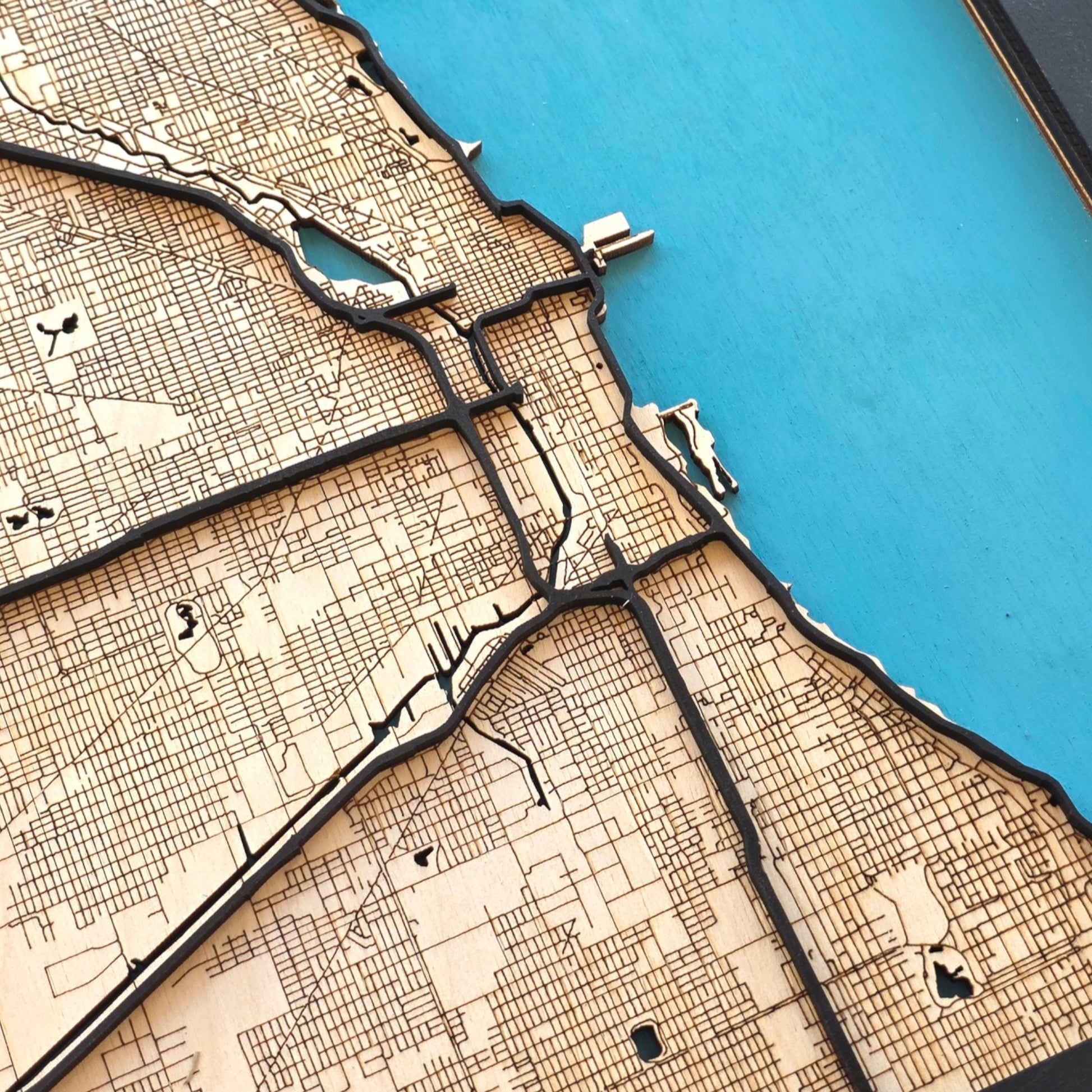 angled close up of Chicago wood map highlighting Lake Michigan shoreline with layered road detail and engraved street grid