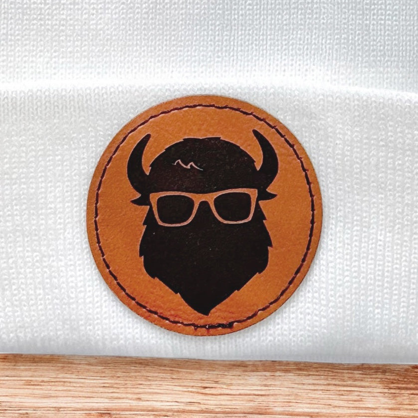 Close up of Curious Bison leatherette patch showing bison head logo with glasses on knit beanie