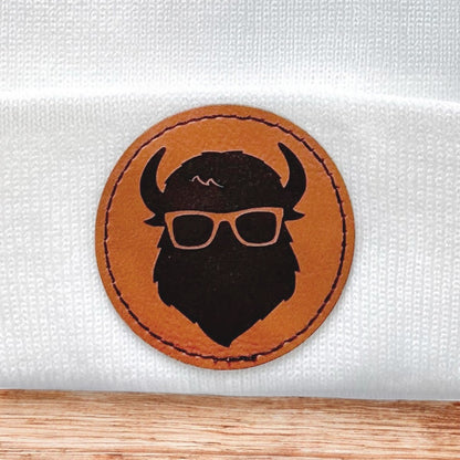 Close up of Curious Bison leatherette patch showing bison head logo with glasses on knit beanie