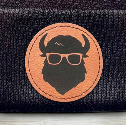 Detailed view of Curious Bison bison logo leatherette patch heat pressed onto black knit beanie