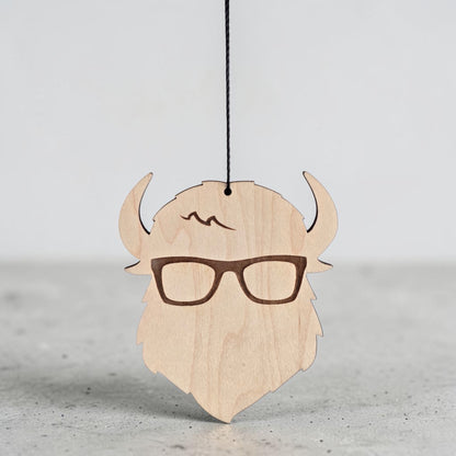 Closeup of Curious Bison wooden ornament hanging by black cord, engraved glasses and logo detail on natural wood decorative ornament