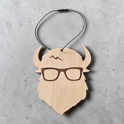 Flat lay of Curious Bison wooden logo ornament with hanging cord on gray surface, wood bison head ornament for holiday decor and Tulsa gift shop souvenir