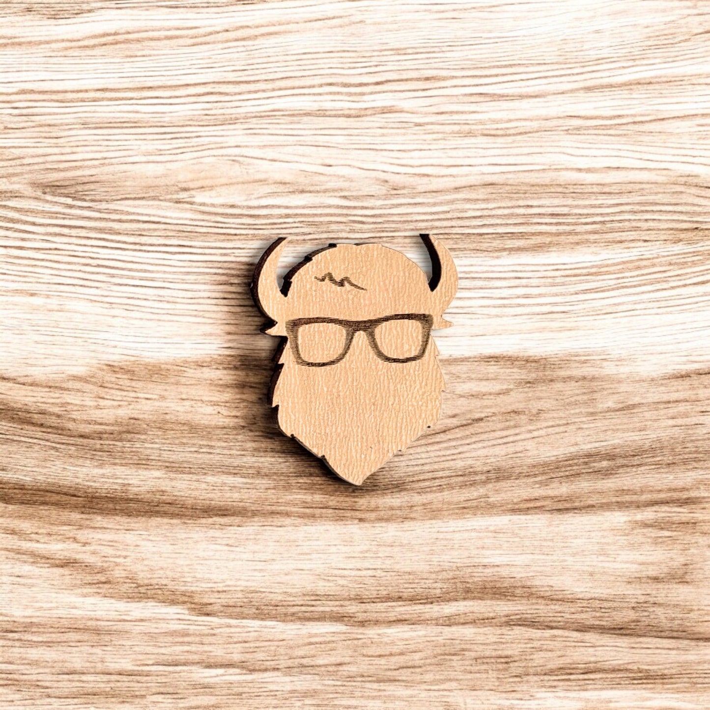 Curious Bison wood pin displayed on wood surface, engraved bison glasses design made from laser cut wood