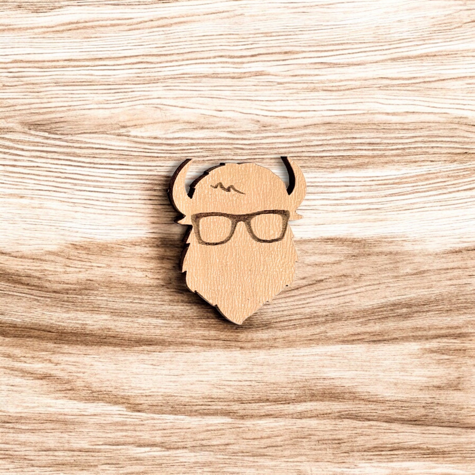 Curious Bison wood pin displayed on wood surface, engraved bison glasses design made from laser cut wood