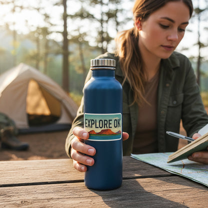 Explore OK license plate vinyl sticker applied to blue metal water bottle at campsite, Oklahoma outdoor travel decal used for camping and road trip gear
