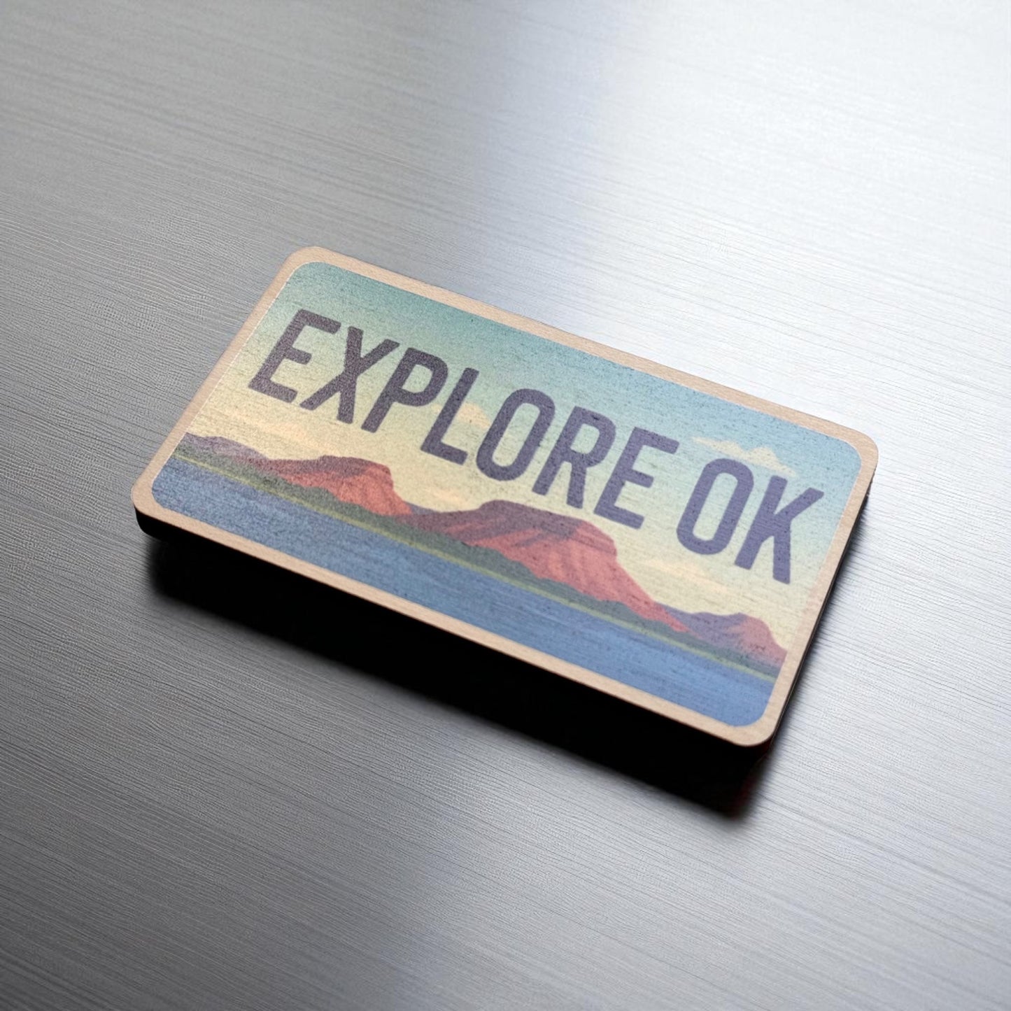 Angled view of Explore Oklahoma wooden magnet showing license plate style shape and colorful landscape artwork, Oklahoma souvenir magnet