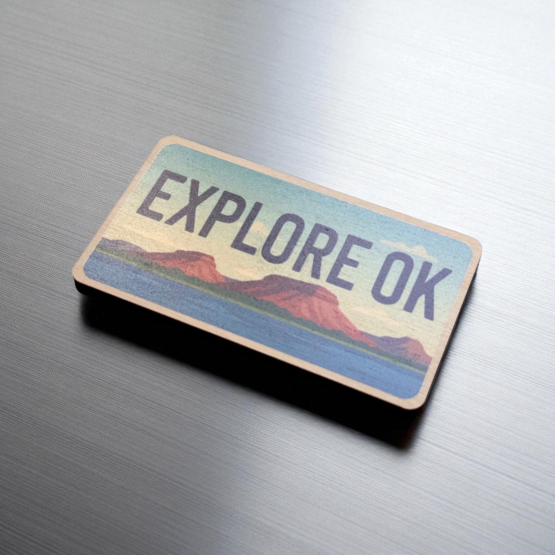 Angled view of Explore Oklahoma wooden magnet showing license plate style shape and colorful landscape artwork, Oklahoma souvenir magnet