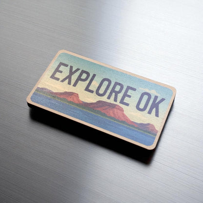 Angled view of Explore Oklahoma wooden magnet showing license plate style shape and colorful landscape artwork, Oklahoma souvenir magnet