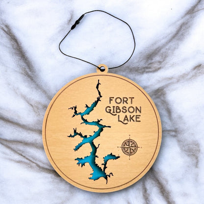 Fort Gibson Lake layered wooden ornament on marble background, laser cut lake shape revealing blue painted water layer, round wood lake ornament with hanging cord
