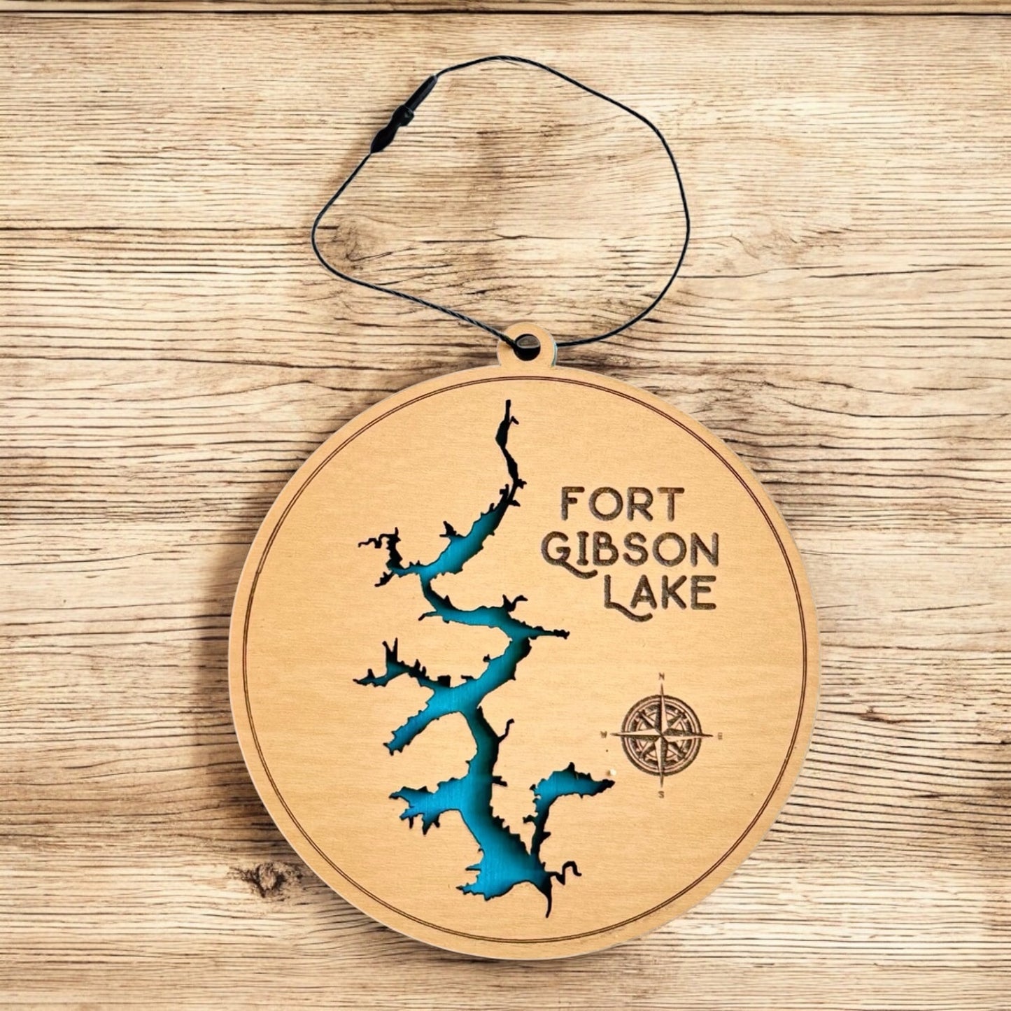 Fort Gibson Lake wooden ornament displayed on wood surface, two layer lake map ornament with painted blue water layer and engraved compass detail