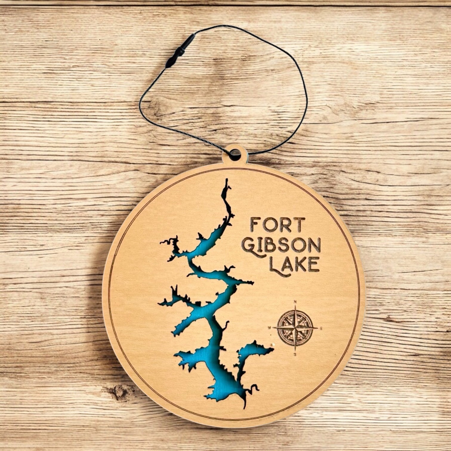Fort Gibson Lake wooden ornament displayed on wood surface, two layer lake map ornament with painted blue water layer and engraved compass detail