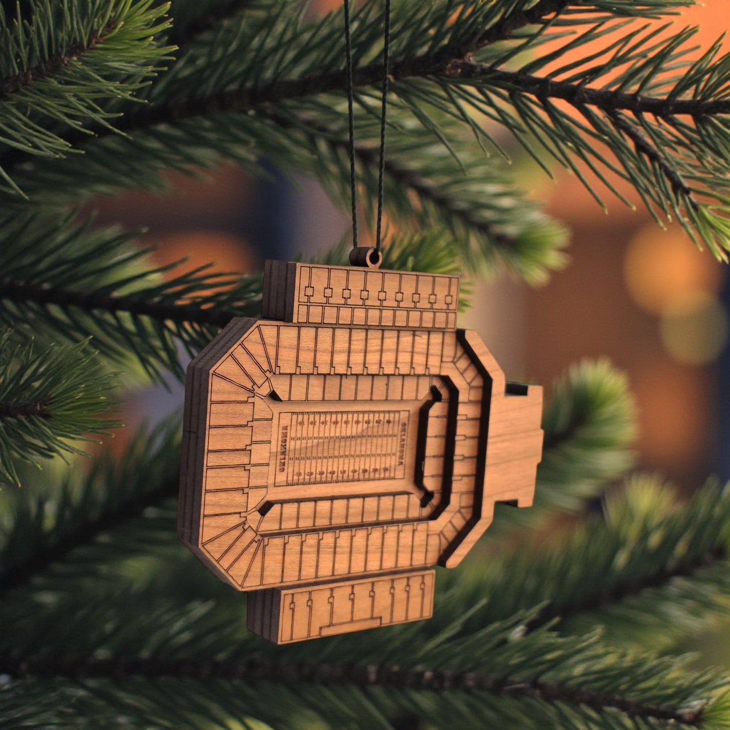 Angled view of Gaylord Family Memorial Stadium wooden ornament hanging from black cord, layered wood OU football stadium ornament for sports fan gift