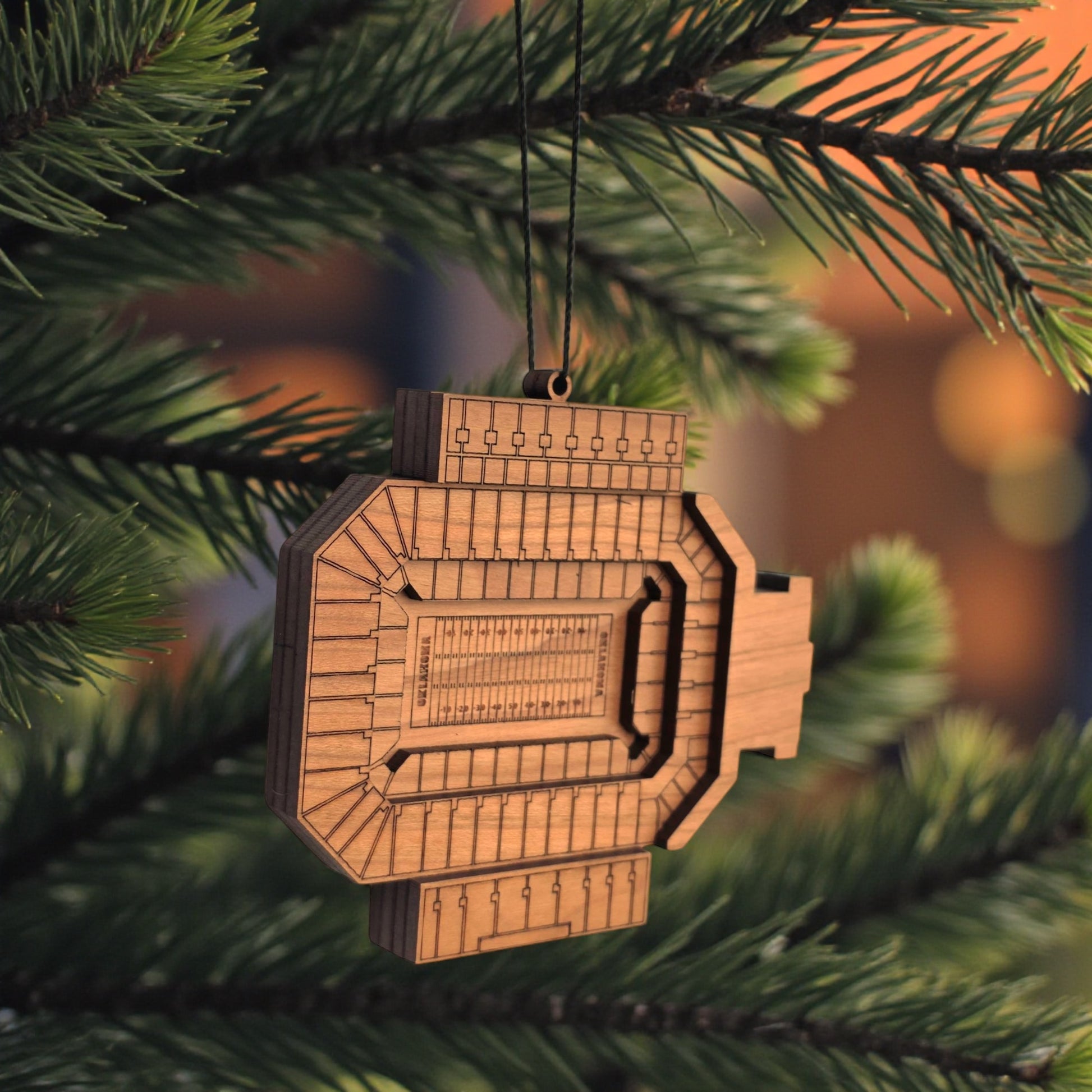 Angled view of Gaylord Family Memorial Stadium wooden ornament hanging from black cord, layered wood OU football stadium ornament for sports fan gift