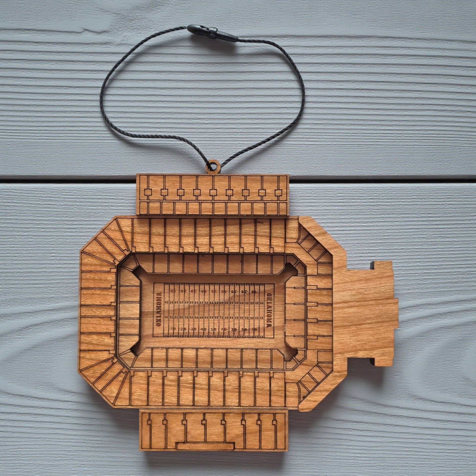 Flat lay of Gaylord Family Memorial Stadium wooden ornament with engraved seating and football field layout, college football stadium ornament made from wood