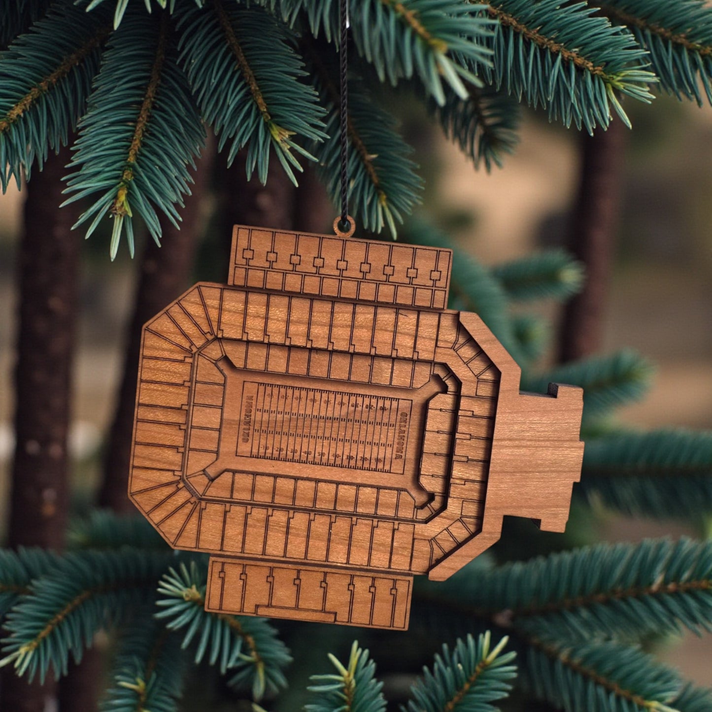 Gaylord Family Memorial Stadium wooden ornament hanging on evergreen tree with lights, laser cut OU football stadium ornament used as college football Christmas decor