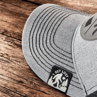 Get Lost Bigfoot aluminum hat clip attached to the brim of a gray hat, engraved Sasquatch hat clip used as hiking or camping accessory