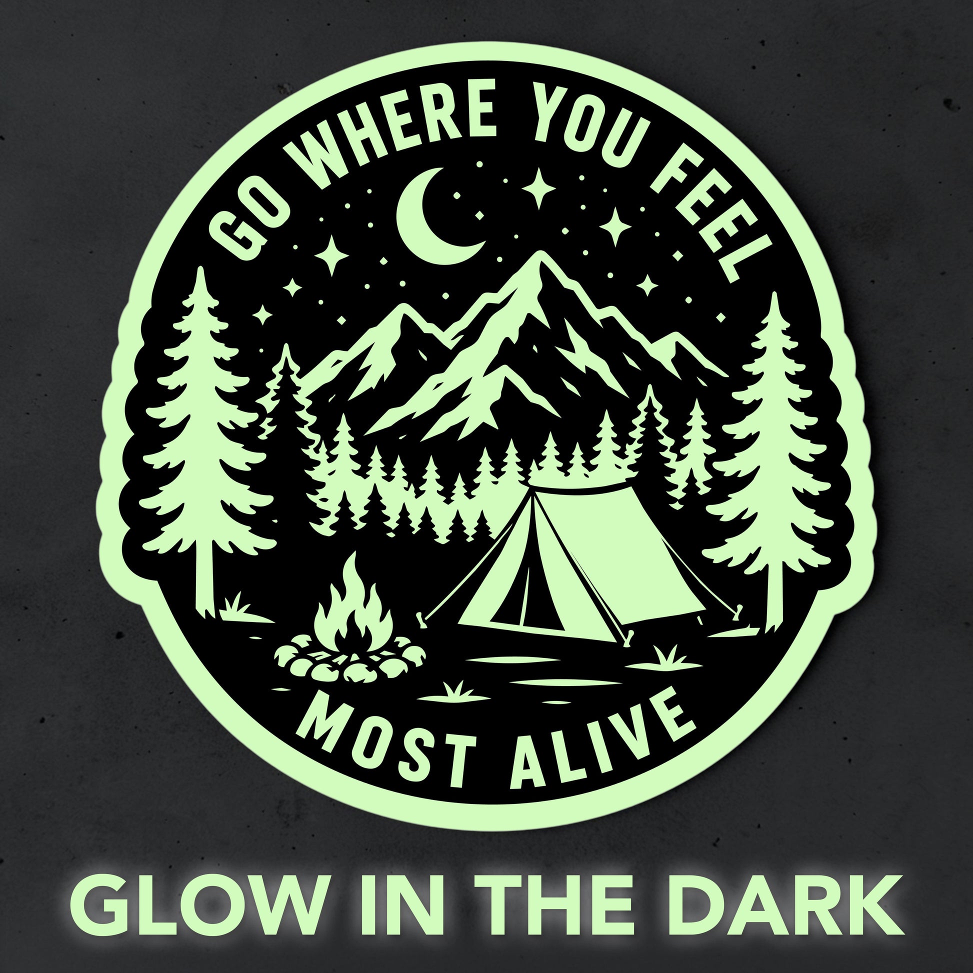 Glow in the dark camping sticker shown glowing pale green against a dark background with mountain, forest, tent and campfire artwork and Go Where You Feel Most Alive text