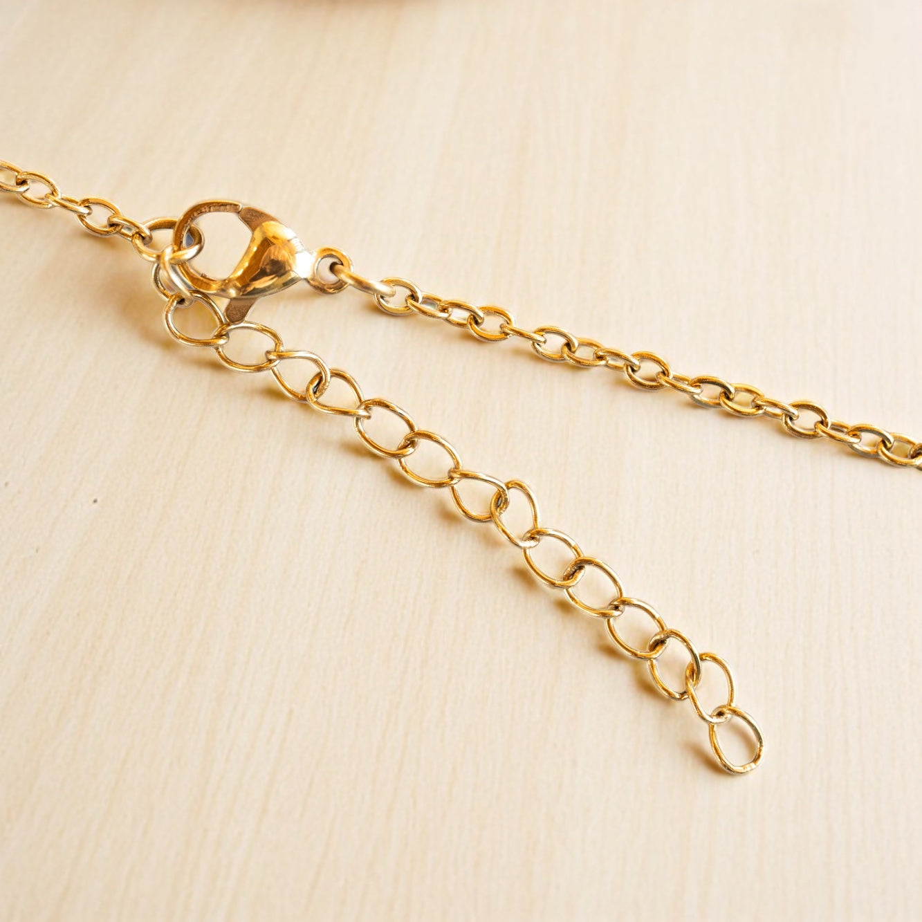 Gold necklace chain extender with lobster clasp on light wood surface