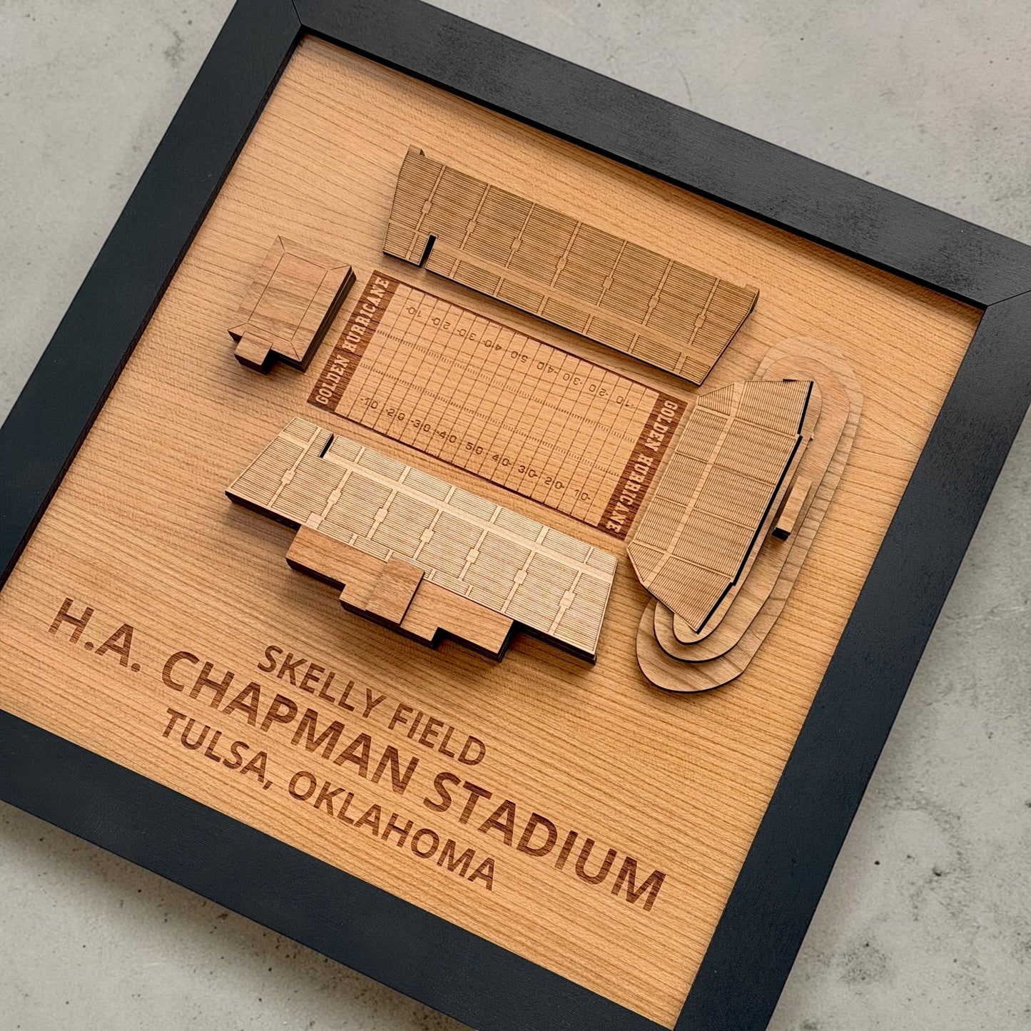 Angled view of layered wood H.A. Chapman Stadium wall art showing engraved seating sections and football field details inside black display frame inspired by Tulsa Golden Hurricane football