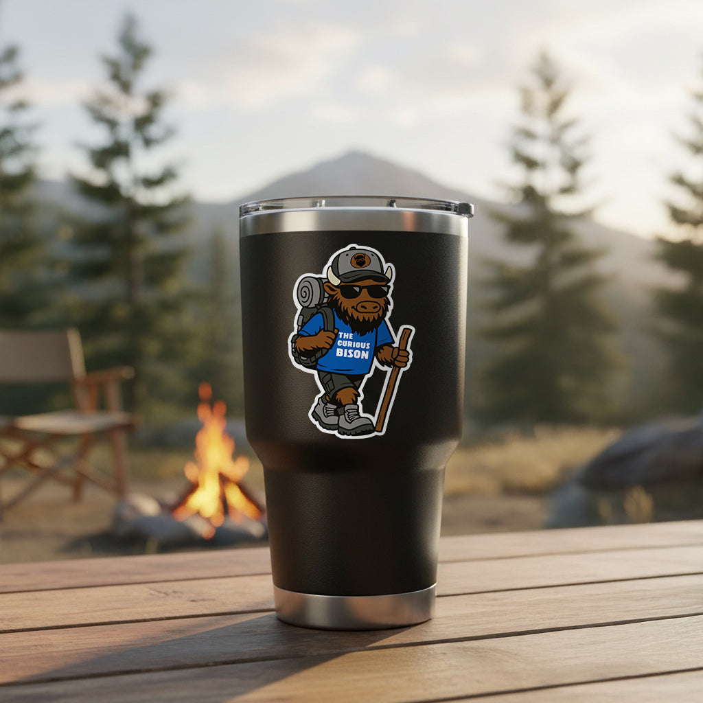 Kerf the Curious Bison hiking mascot sticker applied to insulated tumbler at mountain campsite with campfire and forest background outdoor adventure sticker