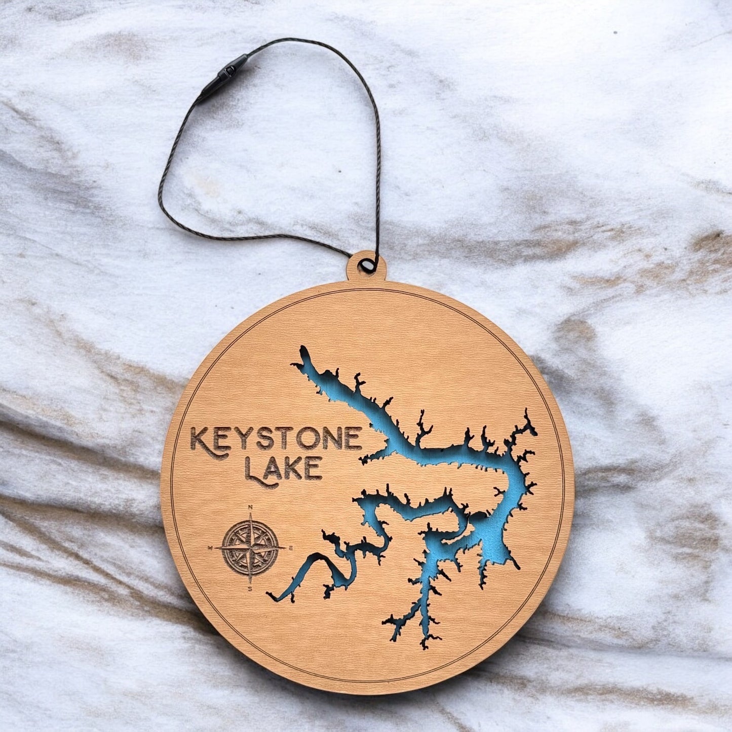Keystone Lake layered wooden ornament displayed on marble surface showing engraved lake name, compass detail, and blue painted water layer