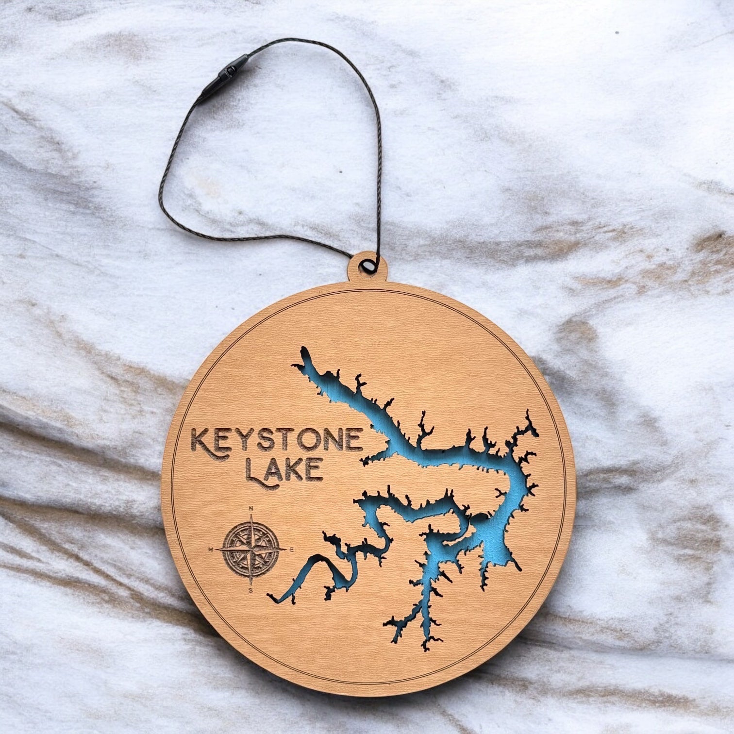 Keystone Lake layered wooden ornament displayed on marble surface showing engraved lake name, compass detail, and blue painted water layer