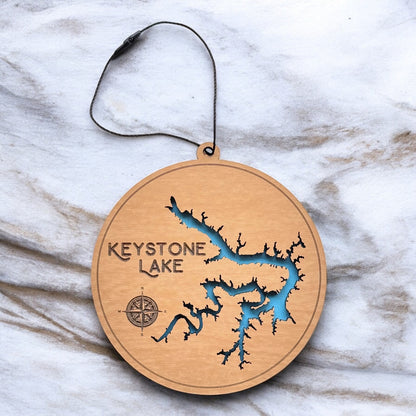 Keystone Lake layered wooden ornament displayed on marble surface showing engraved lake name, compass detail, and blue painted water layer