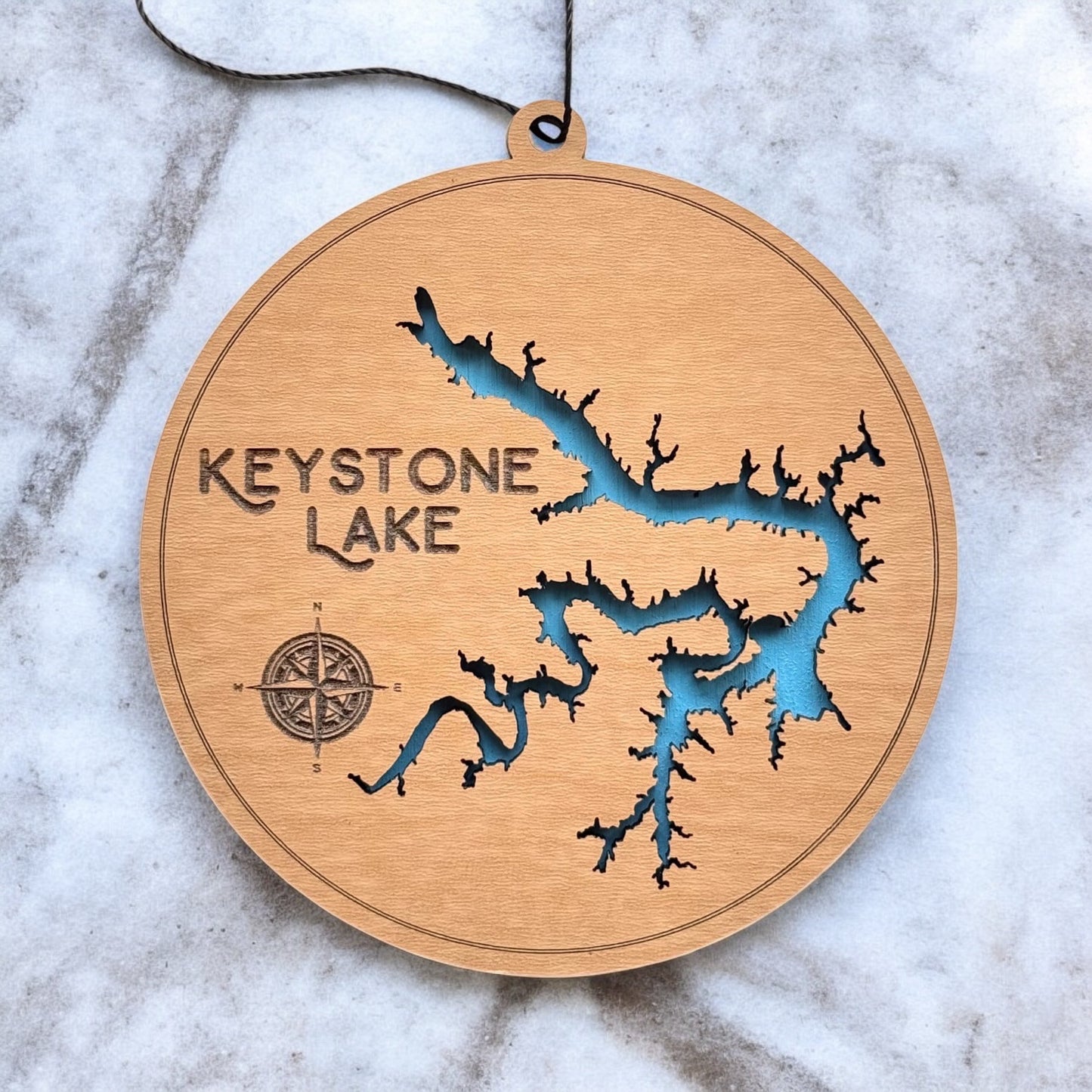 Close up of Keystone Lake wooden map ornament showing laser cut shoreline detail, engraved compass, and painted blue water layer
