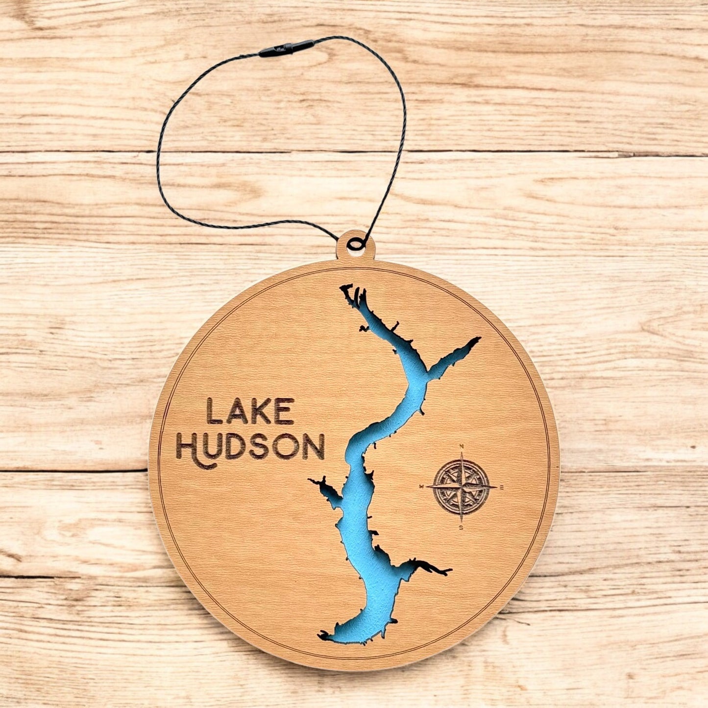 Lake Hudson layered wood ornament shown on wood surface, round lake map ornament with engraved text and blue water detail